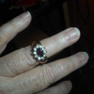 Large Red stone surrounded by a circle of white stones on gold metal